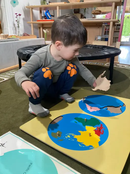 A young boy interacting with a large world map puzzle, learning early geography and spatial concepts.