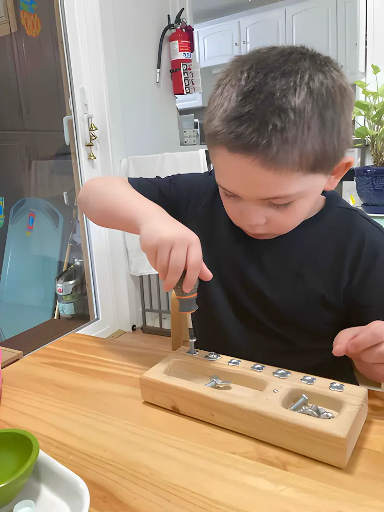 A child using a real child-safe screwdriver to work on a wooden block, developing fine motor skills and hand-eye coordination.