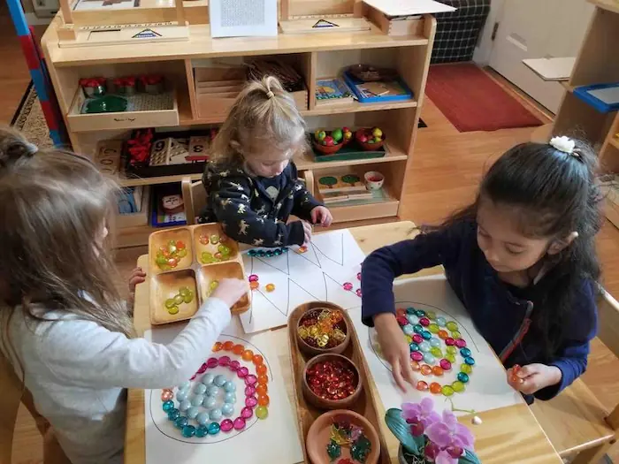 Two girls collaborating to decorate a large drawing with colorful materials, practicing fine motor coordination and teamwork.