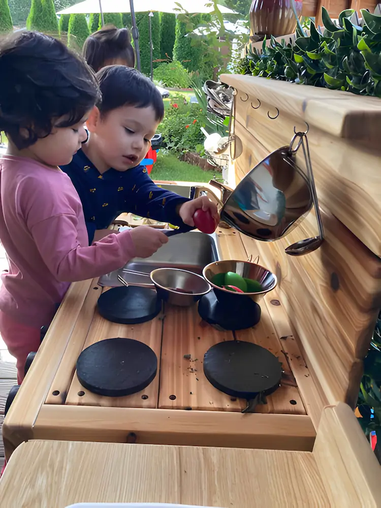 A young boy and girl working together in a child-sized learning kitchen, practicing practical life skills